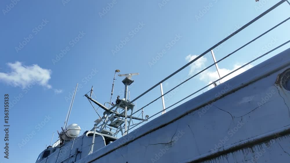 Low-angle view of an aged mechanical structure with rust, bolts, tubing, and cobwebs on a military or industrial ship, set against a clear blue sky. Low-angle view of an aged mechanical structure with rust, bolts, tubing, and cobwebs on a military or industrial ship, set against a clear blue sky.