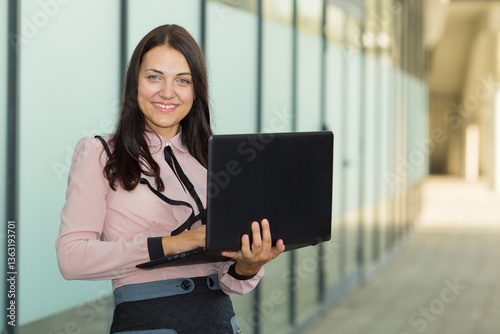 Business woman 30 years old. Woman working with her laptop outdoors next to the office building.