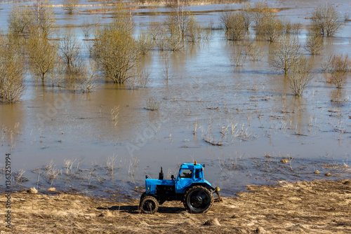 Old blue tractor drives along flooded field in spring, Russia