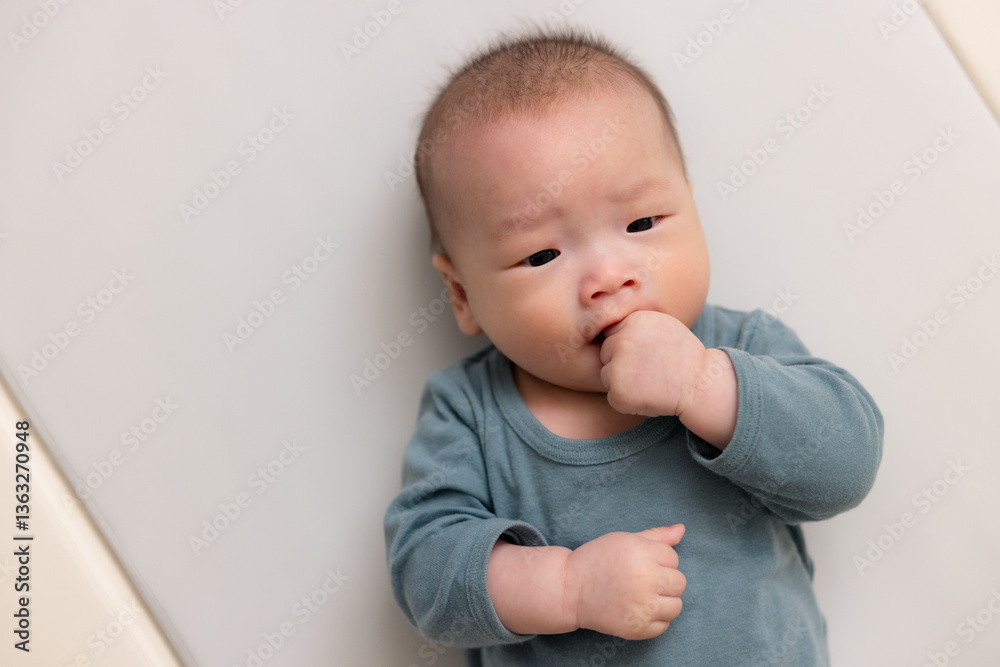Newborn infant sucking fingers while resting indoors