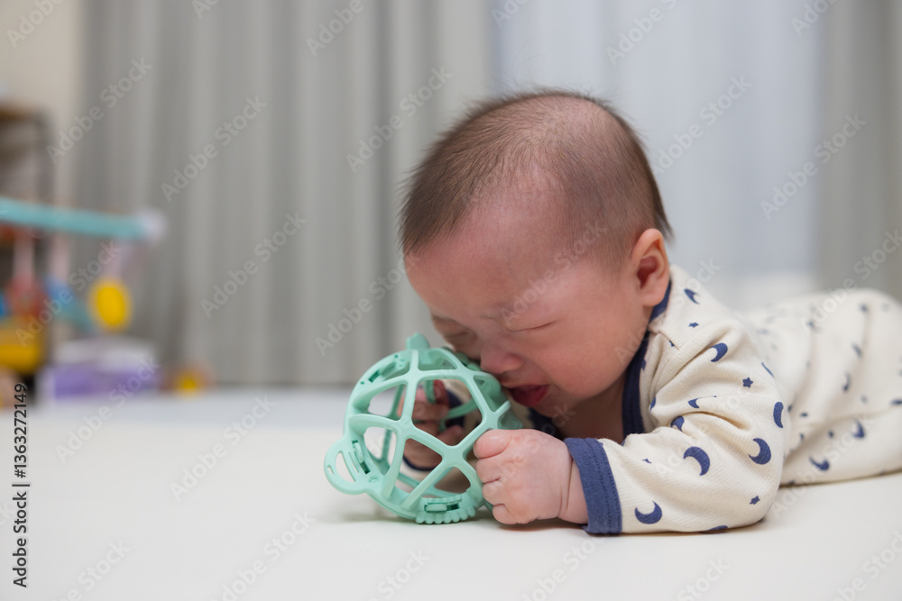 Infant crying and crawling with teether on mat