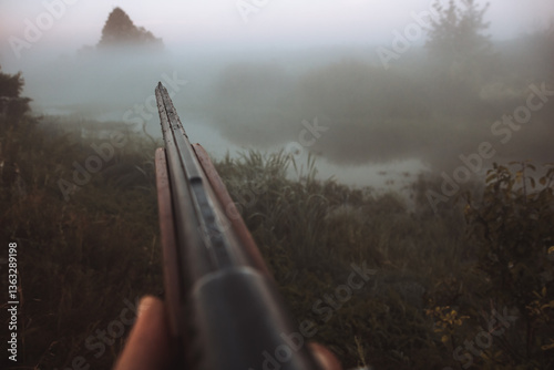Hunting shotgun barrel aiming during foggy morning on river bank during hunting season as hunting background in old vintage style 