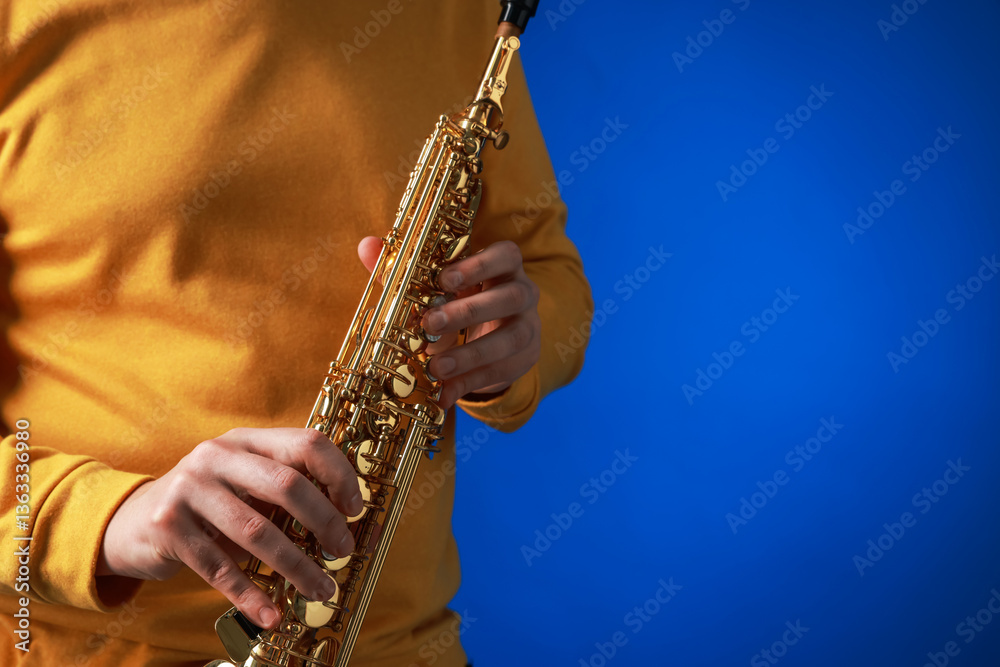 Fototapeta premium Professional musician with soprano saxophone on blue background, closeup. Space for text
