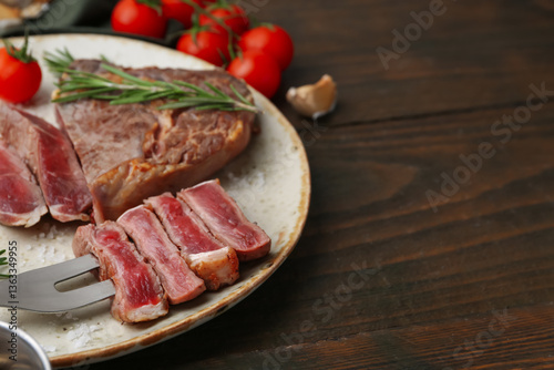 Pieces of delicious beef meat, spices and tomatoes on wooden table, closeup. Space for text