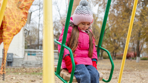Little girl having fun on a swing at the playground on beautiful winter day