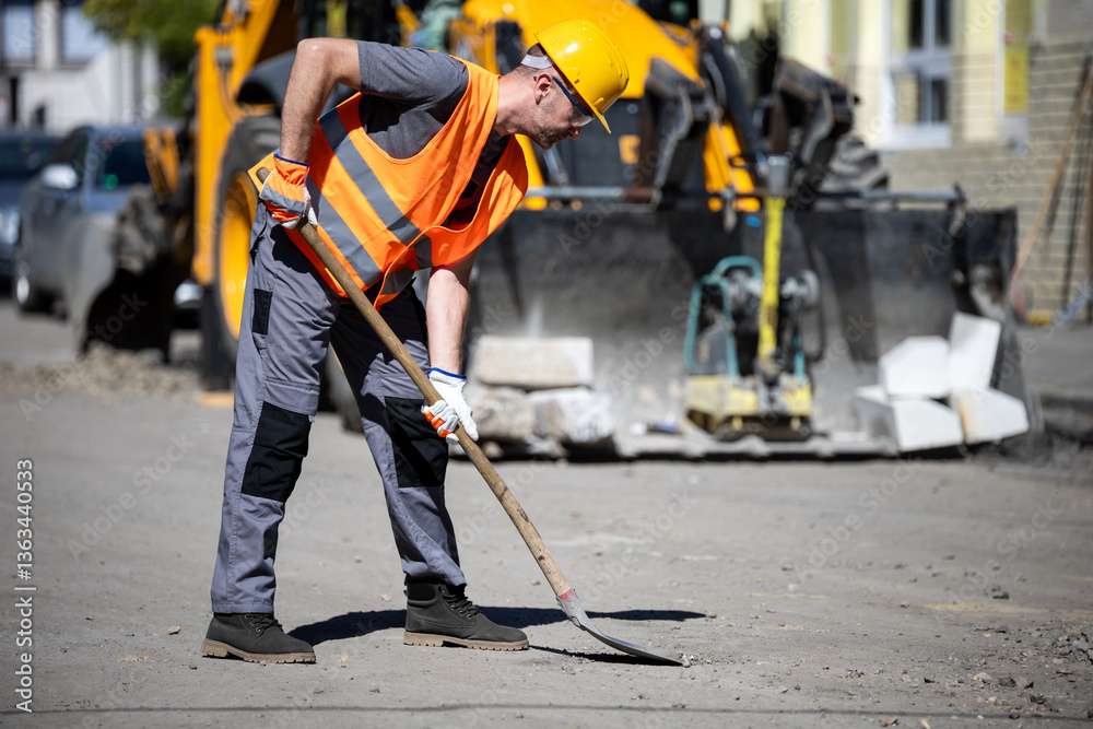 Construction worker digging on an urban street with heavy machinery in the background during daylight hours Construction worker digging on an urban street with heavy machinery in the background during daylight hours