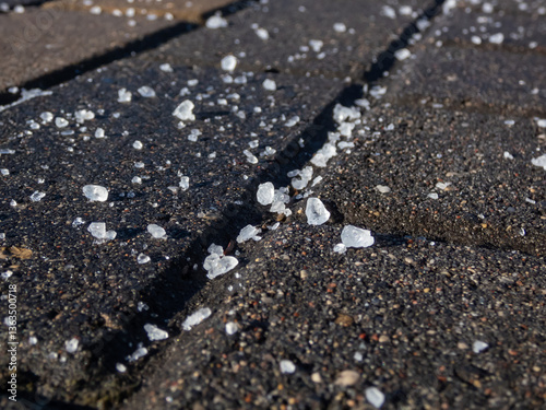 Close-up of white salt grains on icy sidewalk surface in the winter. Applying salt to keep roads clear and people safe in winter