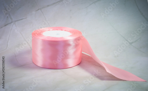 There is a beautiful roll of pink satin ribbon placed on a table