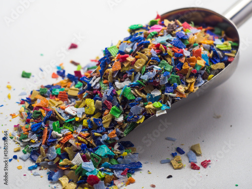 Various colors of plastic waste that has been ground in a stainless shovel on a white background