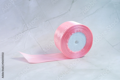 A beautiful roll of pink ribbon is sitting elegantly on a white surface
