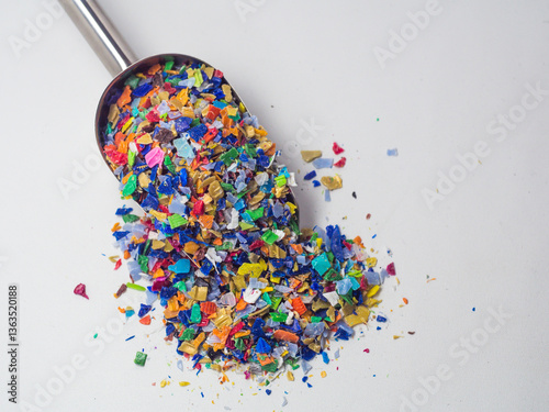 Various colors of plastic waste that has been ground in a stainless shovel on a white background