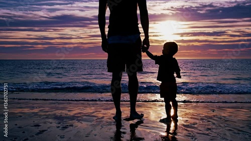 Silhouette of a parent and child holding hands on a beach at sunset. Low-angle shot captures a serene, nostalgic video moment by the sea. Live desktop wallpaper.