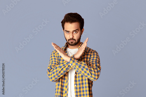 Tableau sur toile Handsome young Indian guy with crossed hands showing stop gesture on violet background