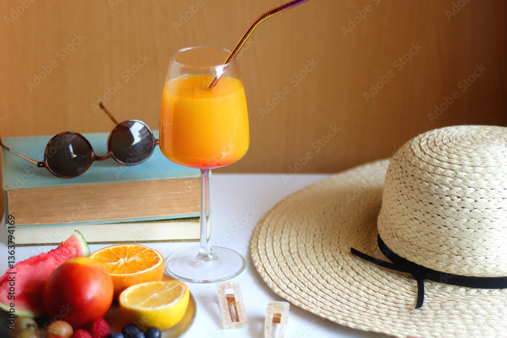 Glass of cocktail, straw hat, sunglasses, books, fresh fruit, chocolate and accessories. Summer essentials on the table. Selective focus.