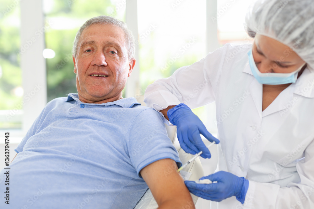 Fototapeta premium Adult woman doctor in medical uniform makes injection in arm of elderly man in medical office