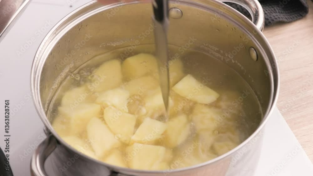 cook is boiling potatoes in a pot of water for mashed potatoes and checking the doneness with a knife. cook is boiling potatoes in a pot of water for mashed potatoes and checking the doneness with a knife.