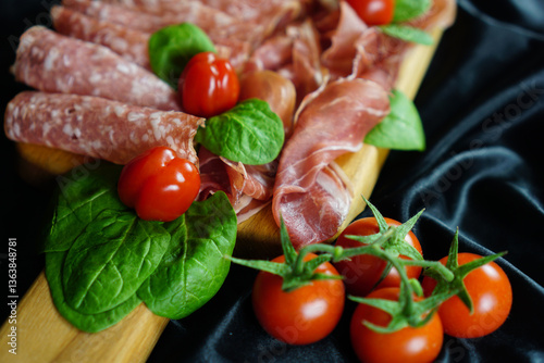 Italian prosciutto slices elegantly arranged on a wooden cutting board with fresh basil leaves and cherry tomatoes on a black satin background, concept of food photography, catering, restaurant menu