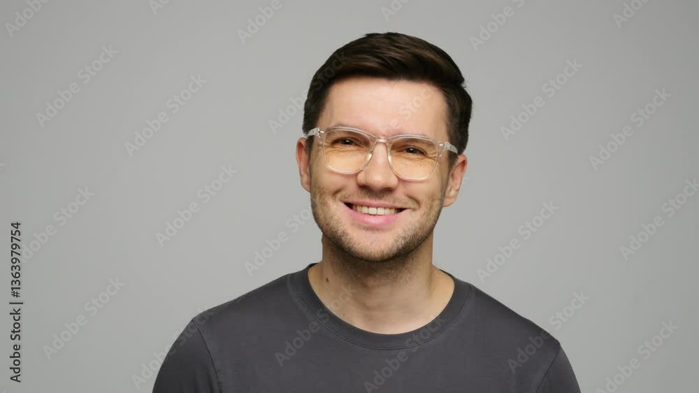 Confident man in glasses showcases a warm smile in a minimalist indoor setting. Confident man in glasses showcases a warm smile in a minimalist indoor setting.