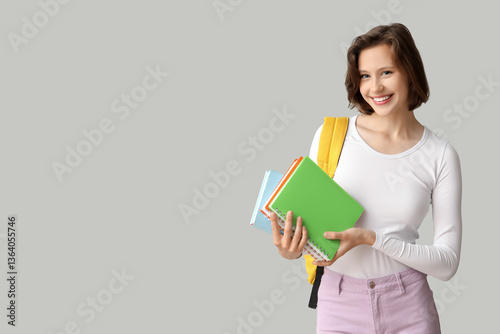 Happy female student with backpack and notebooks on grey background