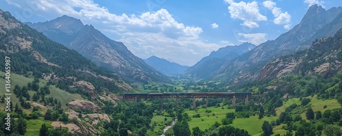 A train traverses a bridge spanning a valley between large mountains