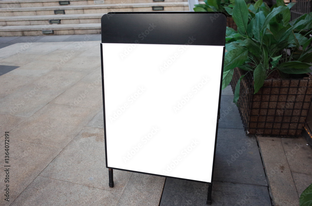 Blank white outdoor advertising stand or sandwich board mock up template. Clear street signage board placed by an outdoor dinning area of a restaurant. Background texture of standee on street.