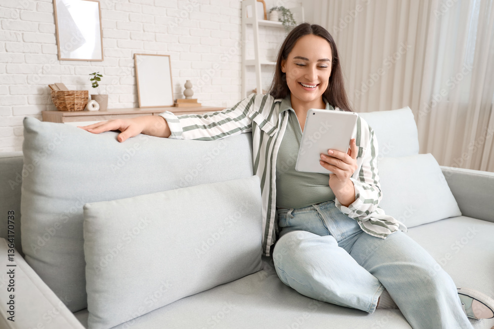 Beautiful woman using tablet computer on couch at home Beautiful woman using tablet computer on couch at home