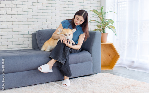 Portrait of asian young beautiful woman happy smile and puppy cute welsh corgi dog sitting on sofa playing funny animals in living room at home, concept embracing lifestyle enjoy trust love pet friend