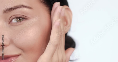 Caucasian female model gently rubs skincare product on cheek while smiling, captured in smooth slow motion. Great for facial cream, cleanser, or luxury beauty product promotions.