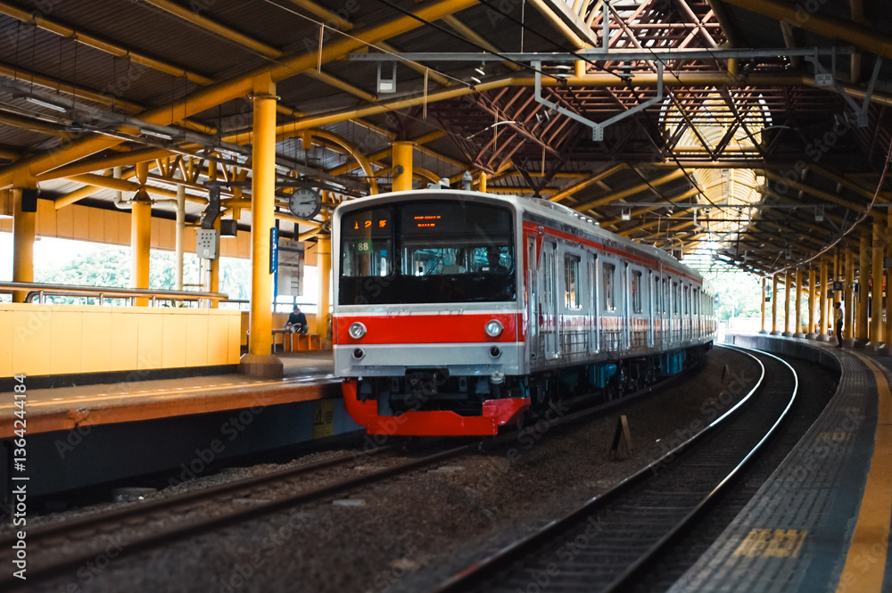 Fototapeta premium the commuter city train slowly entered the station, The train has multiple passenger cars. The train is on a railway track that runs along the platform. Tracks run parallel to one another.