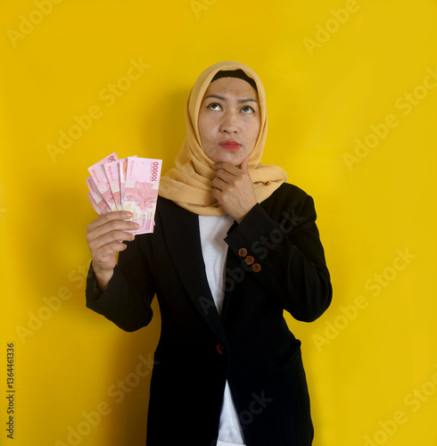 Adult Asian Muslim Businesswoman Doing Thinking Gesture While Holding Indonesia Paper Money photo