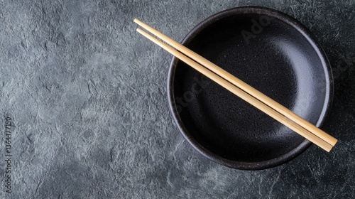 A black bowl with chopsticks set on a textured surface