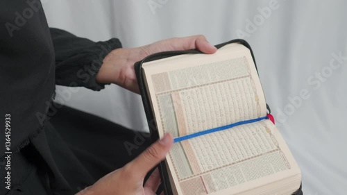 A person holding a black leather bound Quran book with a golden emblem on the cover.