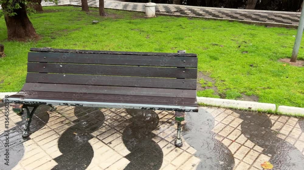Panning view of empty bench in a park in the rain. Daylight