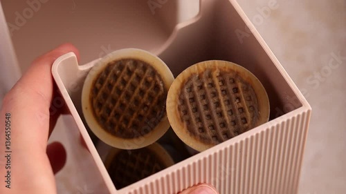 A woman's hand shows the compartment for used capsules from a capsule coffee machine in pale beige, champagne or rose gold. Recyclable plastic coffee capsules with a paper lid
