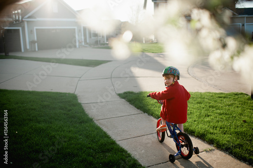 Boy with helmet on rides bike with training wheels down sidewalk