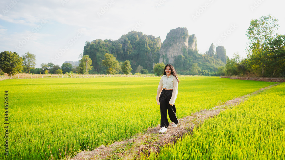 A woman walks through a lush green rice field, framed by towering mountains under a clear sky, embodying tranquility and nature's beauty. A woman walks through a lush green rice field, framed by towering mountains under a clear sky, embodying tranquility and nature's beauty.