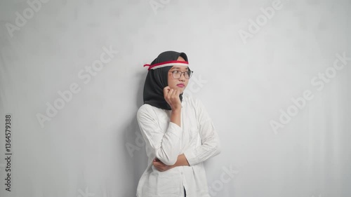 A young asian woman in a hijab and Indonesian flag headband poses, looking at the camera.