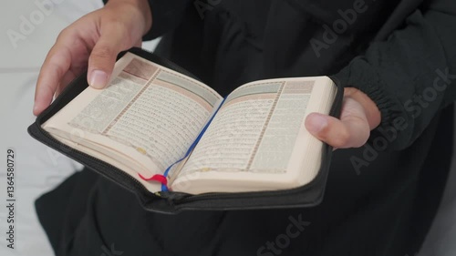 A person's hands gently holding a Quran with a golden emblem.