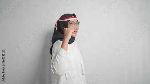 A young asian woman wearing a hijab and glasses with an Indonesian flag headband.