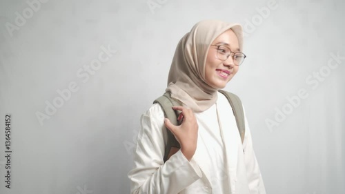 A asian woman in a hijab and glasses looking down against a plain white background.
