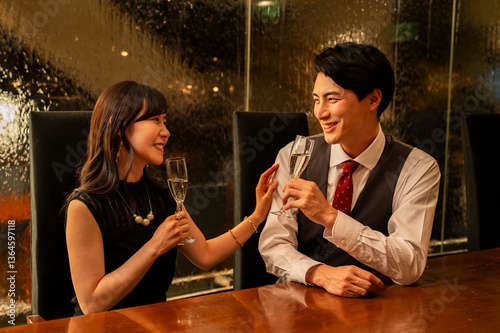 Obraz na płótnie A man and woman dressed formally are smiling at each other while toasting with champagne glasses. They are seated across from each other at a wooden bar with warm ambient lighting. w salonie