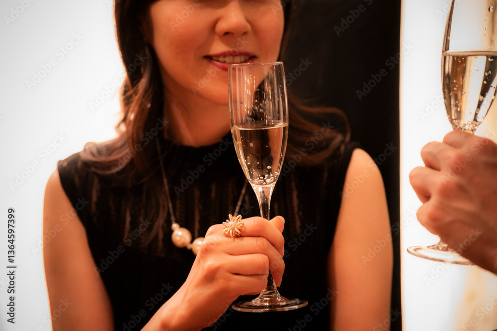 A woman in a sleeveless black dress smiles while holding a champagne glass at an upscale bar. The warm lighting and her elegant accessories convey a festive, celebratory mood.
Keywords: