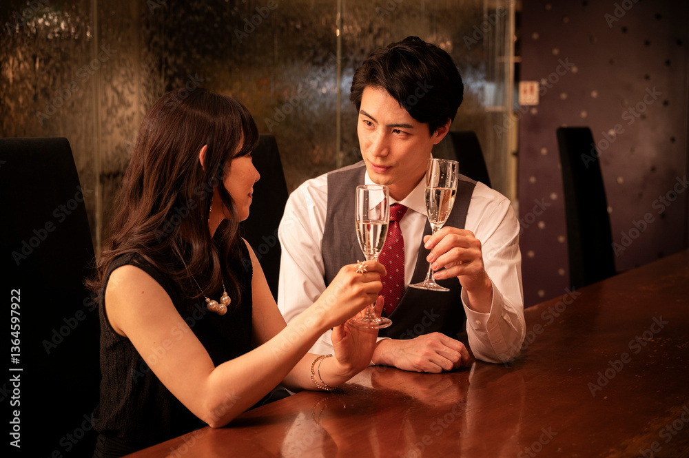 A couple dressed in formal attire clinks champagne glasses in a warm, romantic bar setting. Their smiles reflect joy and connection, emphasizing a mood of celebration.