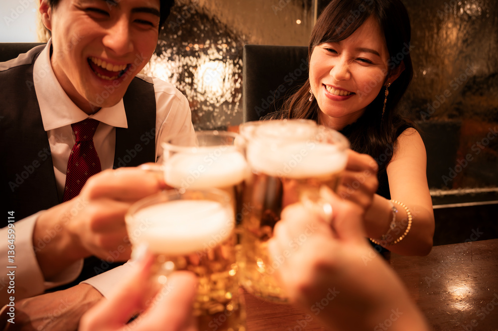 A cheerful man and woman laugh and smile as they clink their beer mugs with friends in a warmly lit bar. The image captures a candid, festive moment of togetherness and joy.