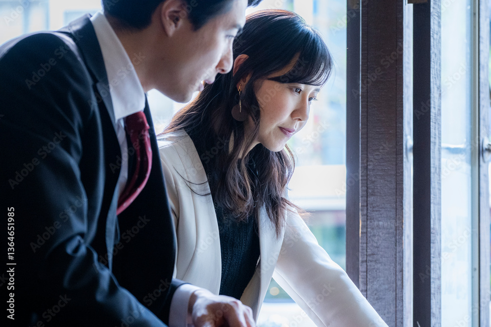 A businessman and a businesswoman in formal attire have a serious conversation while seated by the window at a modern café. Natural light highlights their focused expressions as they engage in a profe
