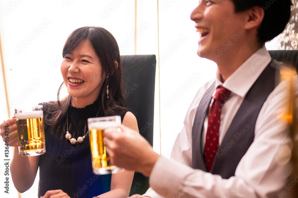 A smiling woman dressed elegantly in black raises her beer mug in a cheerful toast at a warmly lit bar. Her pearl necklace and statement earrings add a touch of luxury to the lively, social atmosphere