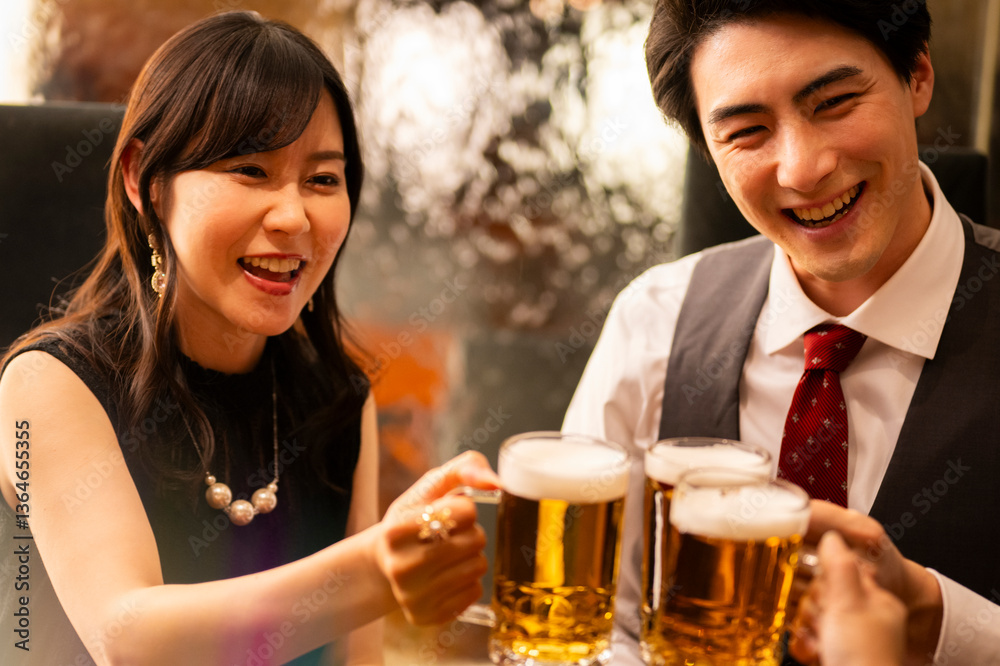 A smiling man and woman enjoy a moment of celebration with beer at a sleek bar. The man wears a white shirt with a red tie and vest, and the woman smiles warmly as they toast.