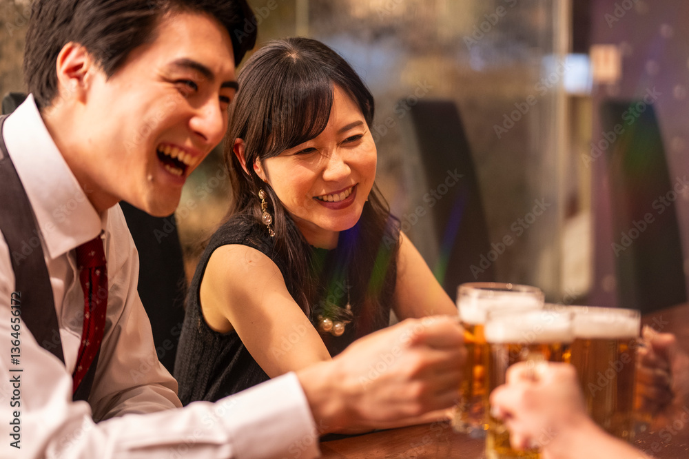 A joyful group of 4 friends toasts with beer mugs while sitting at a polished wooden bar. The ambient lighting and formal clothing suggest a special celebration or social gathering.
