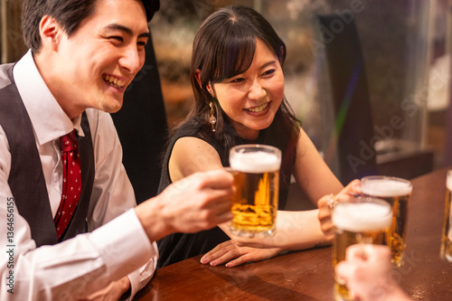 Obraz na płótnie A joyful group of 4 friends toasts with beer mugs while sitting at a polished wooden bar. The ambient lighting and formal clothing suggest a special celebration or social gathering. w salonie