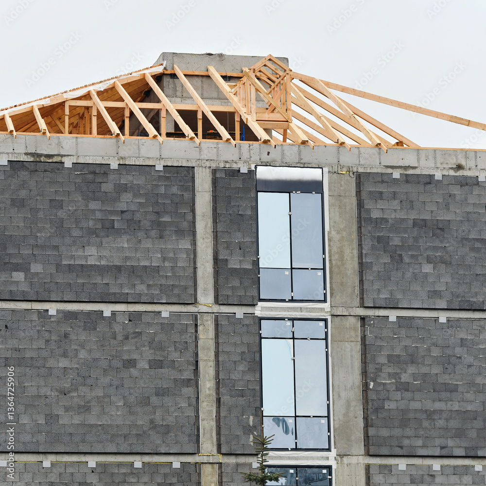 Construction site featuring modern building in progress with roof installation, window fitting, and insulation work to ensure energy efficiency and durability. Roof rafters installation
